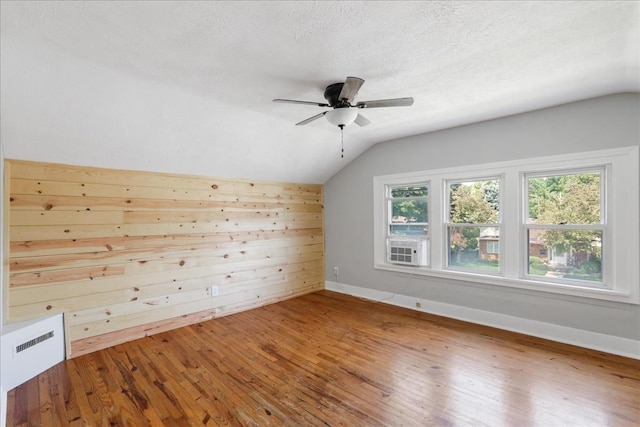 additional living space featuring a textured ceiling, vaulted ceiling, ceiling fan, wooden walls, and hardwood / wood-style floors