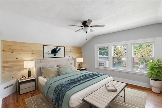 bedroom featuring hardwood / wood-style floors, wood walls, lofted ceiling, ceiling fan, and a textured ceiling