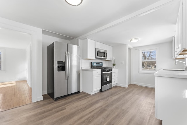 kitchen with white cabinets, appliances with stainless steel finishes, beamed ceiling, light hardwood / wood-style floors, and sink