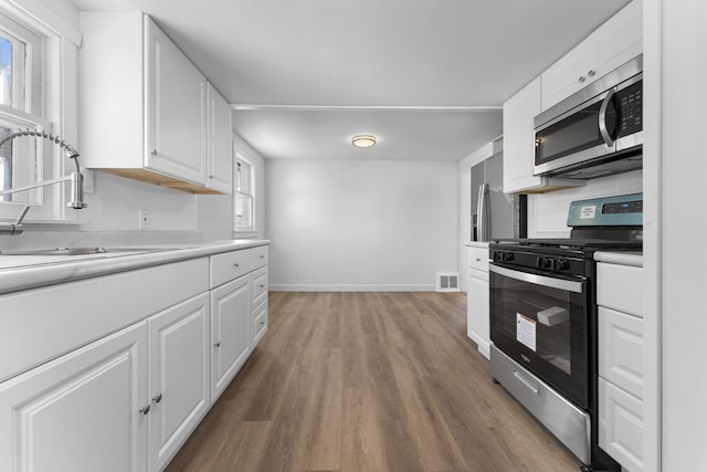 kitchen with white cabinetry, hardwood / wood-style flooring, appliances with stainless steel finishes, backsplash, and sink