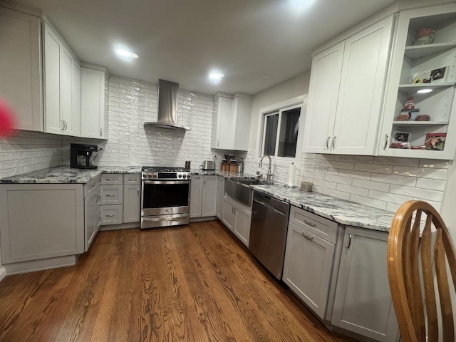 kitchen with backsplash, sink, appliances with stainless steel finishes, and wall chimney range hood