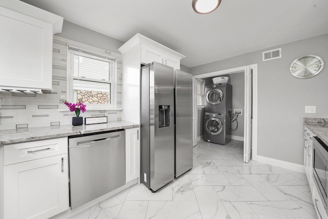 kitchen featuring white cabinetry, stacked washing maching and dryer, light stone countertops, and stainless steel appliances