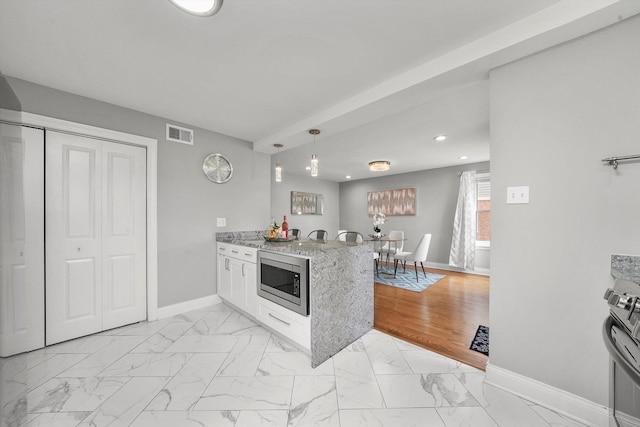 kitchen featuring pendant lighting, kitchen peninsula, light stone countertops, white cabinetry, and stainless steel appliances