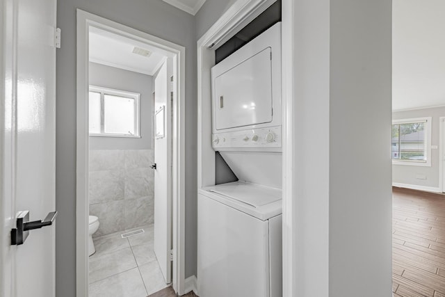 washroom featuring stacked washer / dryer, light tile patterned floors, tile walls, and ornamental molding