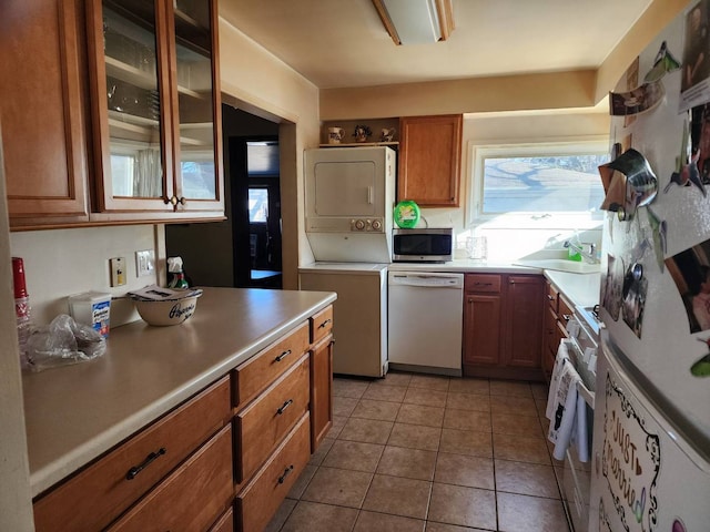 kitchen featuring stacked washer and dryer, dishwasher, sink, and light tile patterned floors