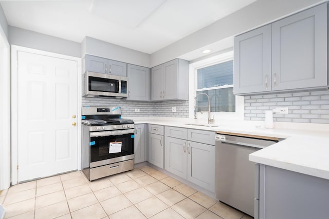 kitchen with sink, decorative backsplash, gray cabinets, light tile patterned floors, and appliances with stainless steel finishes