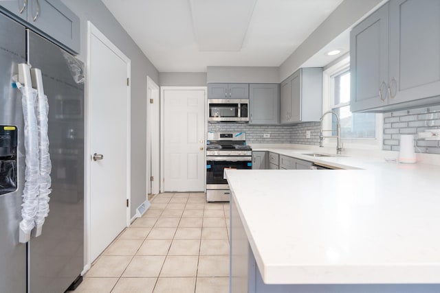 kitchen featuring kitchen peninsula, appliances with stainless steel finishes, tasteful backsplash, sink, and light tile patterned flooring