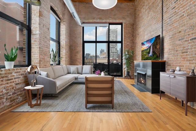 living room featuring a high ceiling, brick wall, and light hardwood / wood-style floors