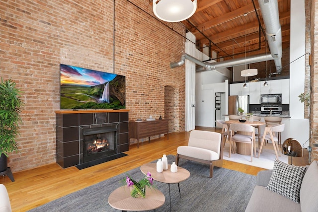 living room with brick wall, hardwood / wood-style floors, a tiled fireplace, a high ceiling, and wooden ceiling