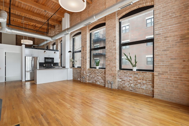 unfurnished living room featuring a towering ceiling, brick wall, and light wood-type flooring