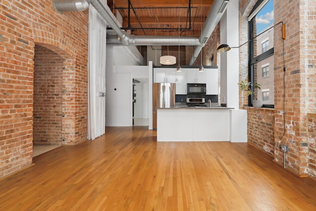 kitchen with pendant lighting, light hardwood / wood-style flooring, a towering ceiling, stainless steel appliances, and white cabinets