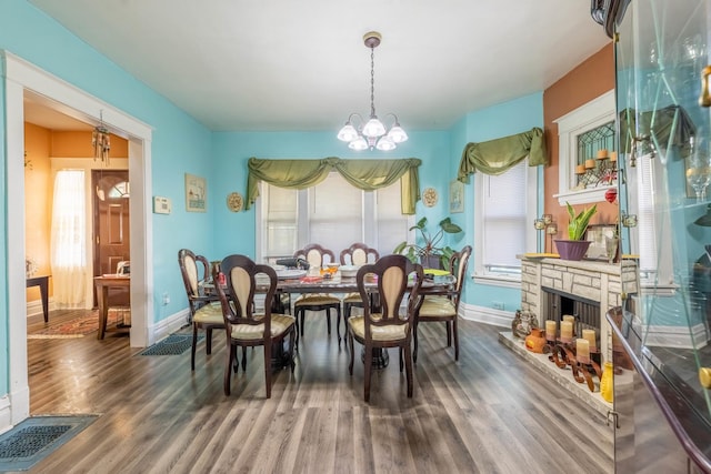 dining area featuring a stone fireplace, plenty of natural light, a notable chandelier, and dark wood-type flooring