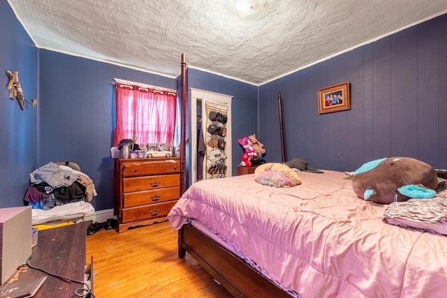 bedroom with a textured ceiling, light hardwood / wood-style floors, crown molding, and wooden walls