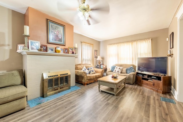 living room with a brick fireplace, ceiling fan, and wood-type flooring