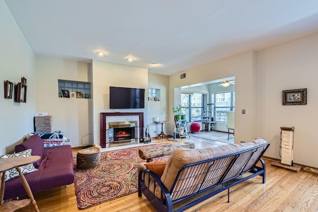 living room featuring a fireplace, light wood-type flooring, and ceiling fan