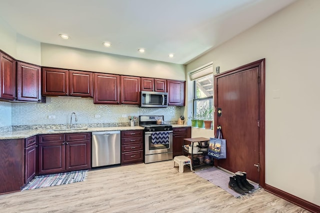 kitchen with light stone countertops, decorative backsplash, stainless steel appliances, sink, and light hardwood / wood-style floors