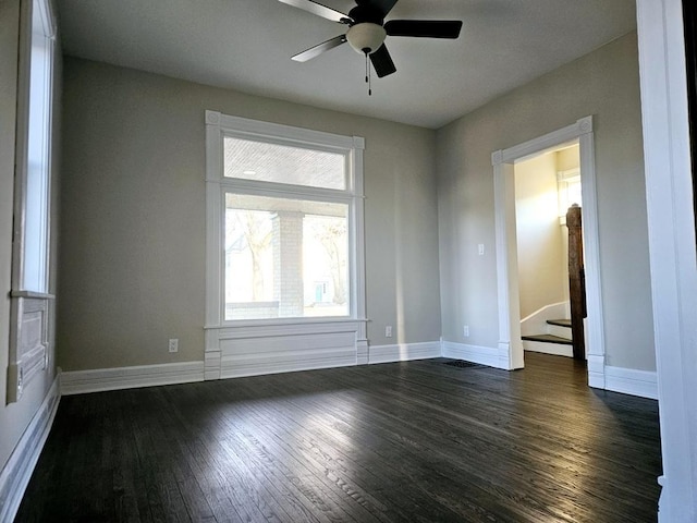 empty room with a ceiling fan, baseboards, dark wood finished floors, and stairs