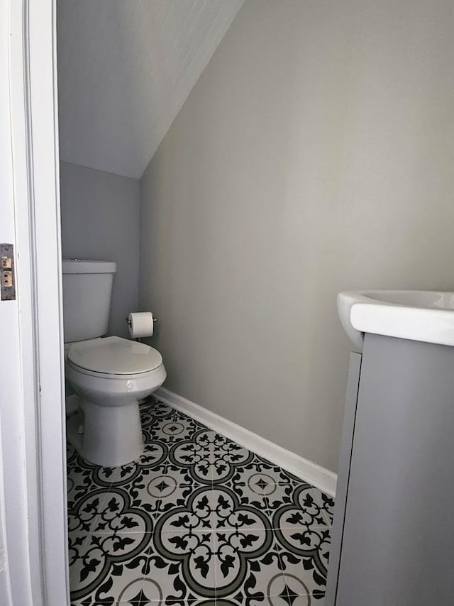 bathroom with toilet, vaulted ceiling, and baseboards