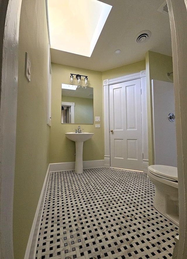 bathroom with toilet, a skylight, and tile patterned floors