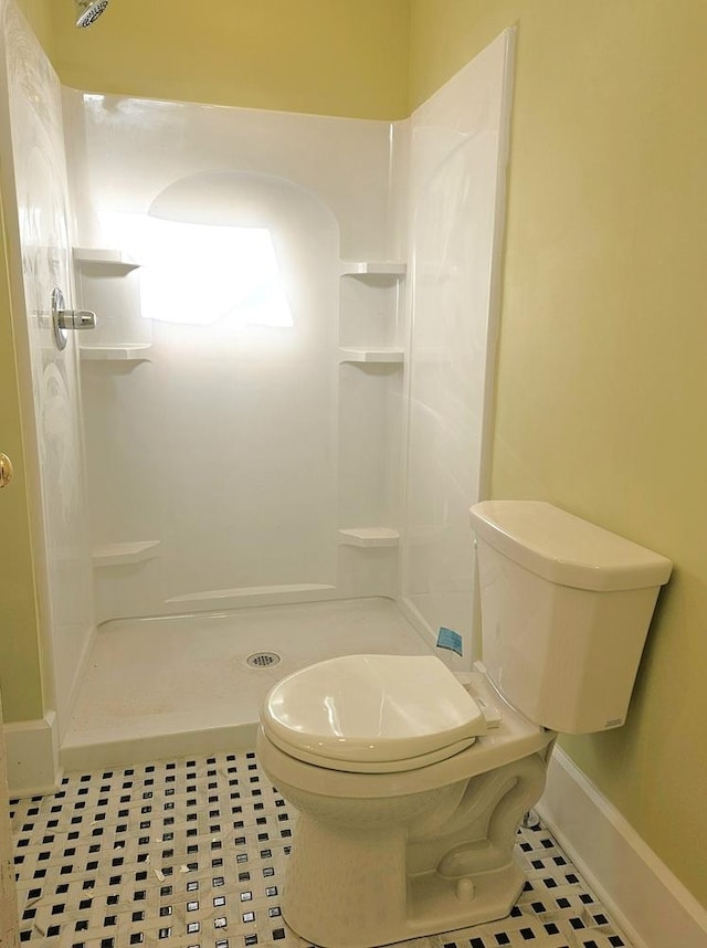 bathroom featuring toilet, a shower stall, baseboards, and tile patterned flooring