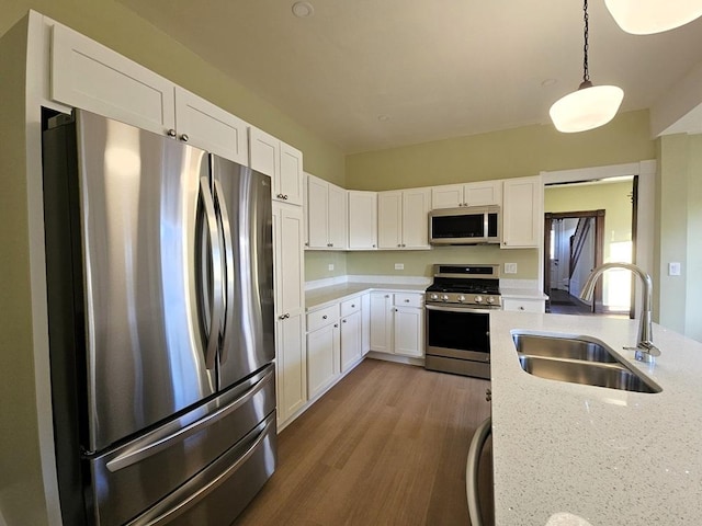 kitchen with decorative light fixtures, sink, light stone countertops, stainless steel appliances, and white cabinets