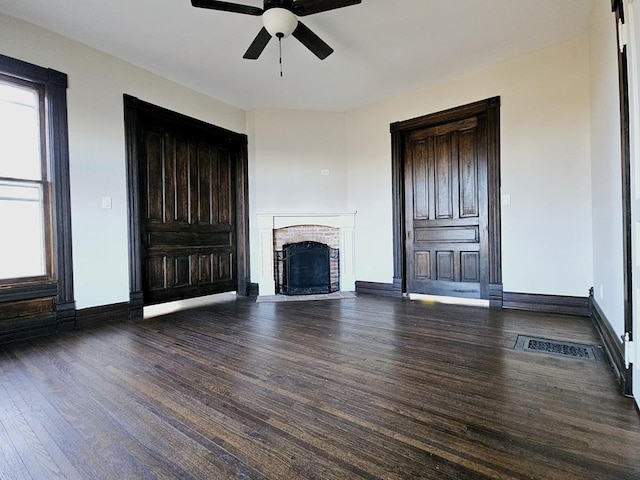 unfurnished living room with a fireplace, ceiling fan, and dark hardwood / wood-style flooring