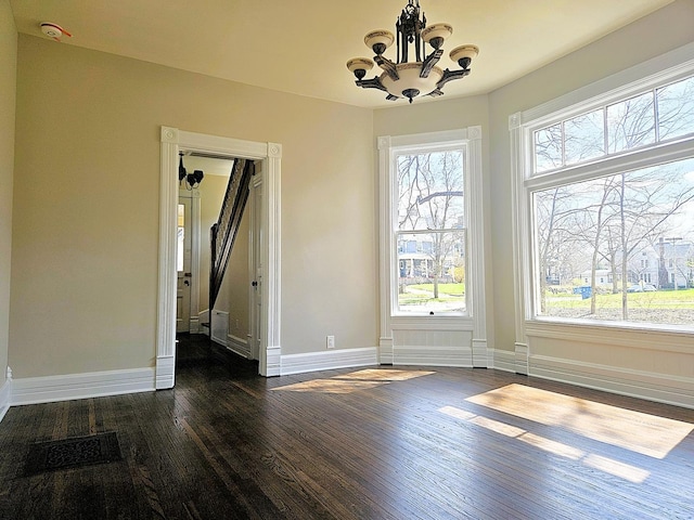 unfurnished dining area featuring dark wood-style flooring, visible vents, baseboards, and an inviting chandelier