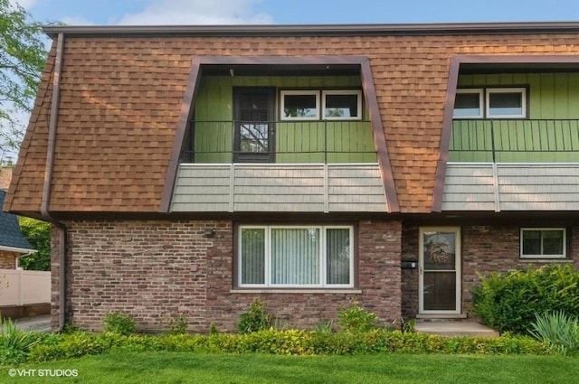 back of property featuring brick siding, a balcony, mansard roof, and roof with shingles