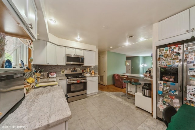 kitchen with visible vents, a sink, white cabinetry, stainless steel appliances, and decorative backsplash