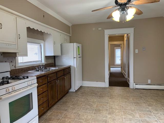 kitchen with tasteful backsplash, a baseboard heating unit, sink, white appliances, and white cabinets