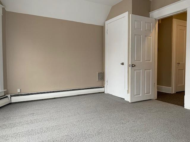 spare room featuring carpet floors, vaulted ceiling, and baseboard heating