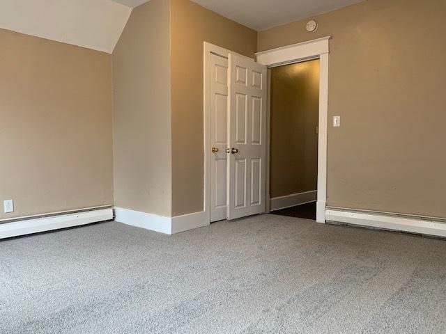 spare room with a baseboard heating unit, carpet flooring, and vaulted ceiling