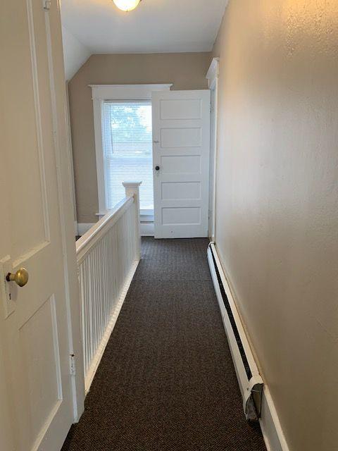 hall featuring vaulted ceiling, dark colored carpet, and baseboard heating