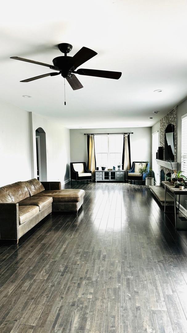 living room with hardwood / wood-style floors, ceiling fan, and a stone fireplace