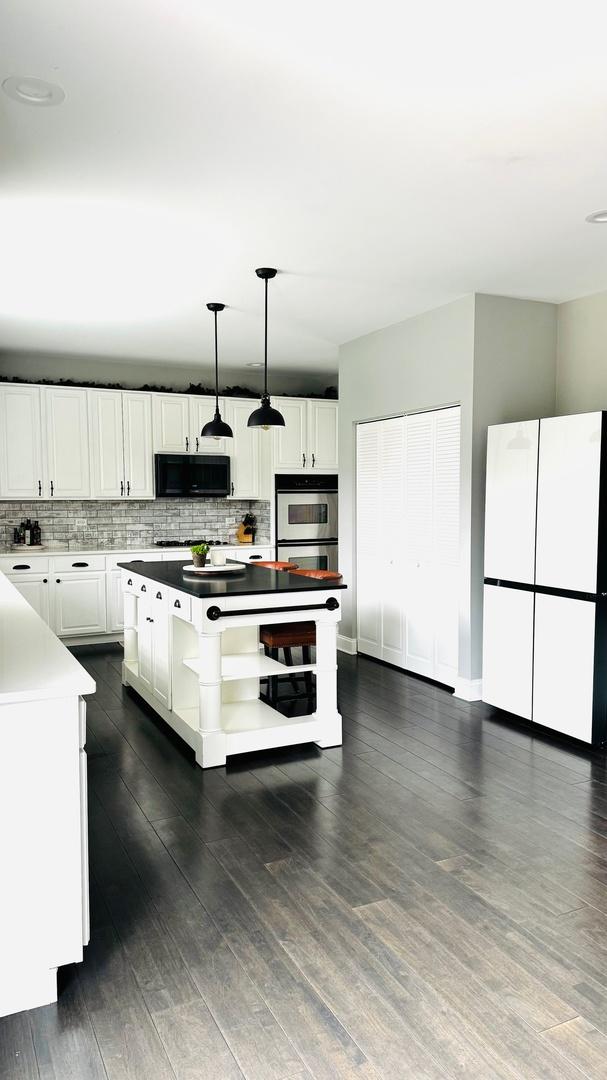 kitchen with decorative backsplash, white cabinets, stainless steel double oven, and hanging light fixtures