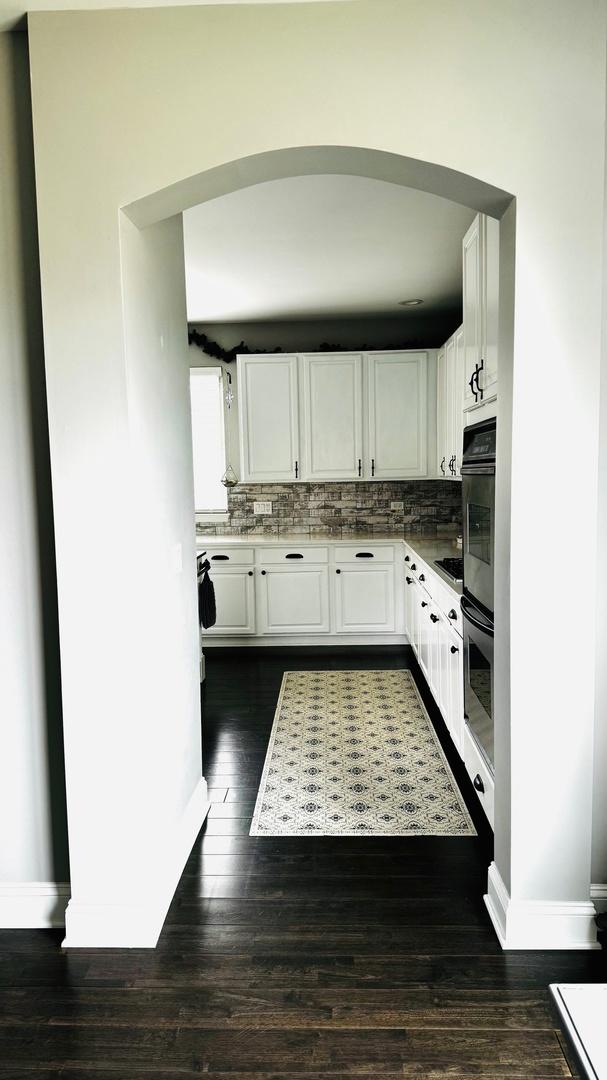 kitchen with double oven, dark hardwood / wood-style floors, tasteful backsplash, and white cabinetry