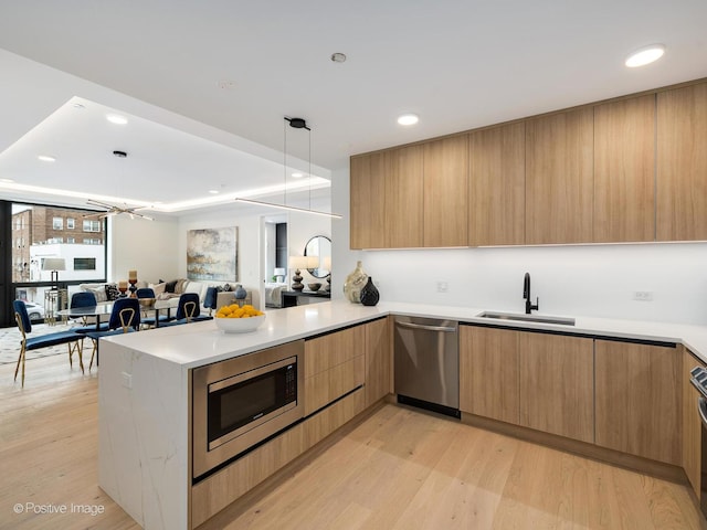 kitchen featuring kitchen peninsula, sink, light wood-type flooring, and appliances with stainless steel finishes