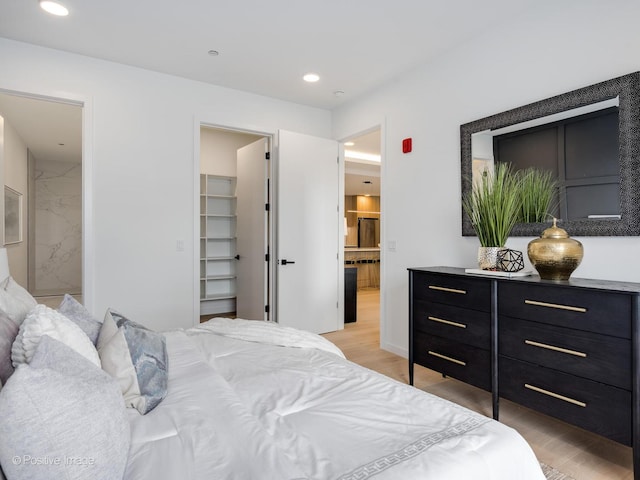 bedroom with ensuite bath, a walk in closet, and light hardwood / wood-style flooring