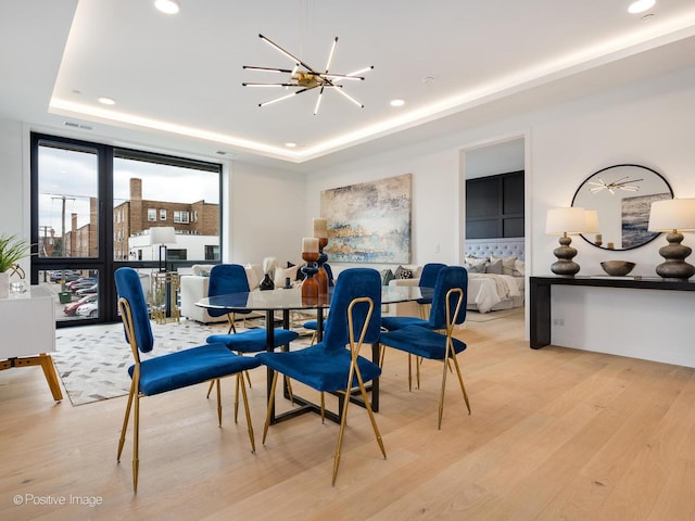 dining room with light wood-type flooring, a raised ceiling, and a notable chandelier