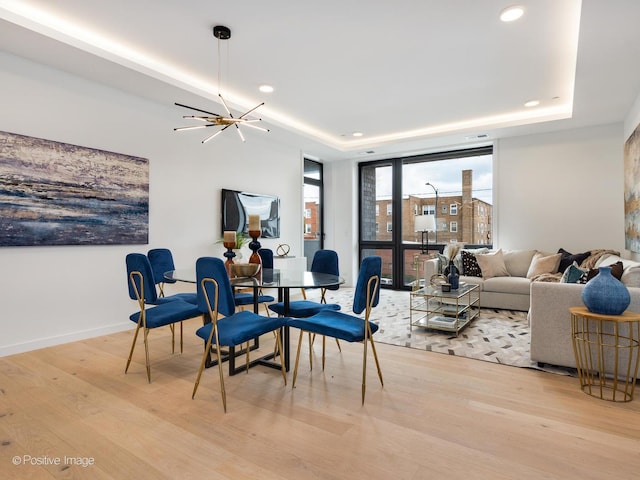 dining area featuring an inviting chandelier, a raised ceiling, and light hardwood / wood-style flooring