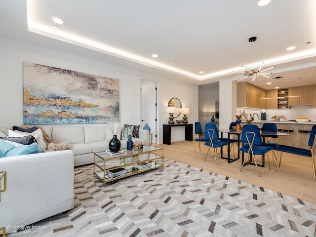 living room featuring a notable chandelier, light hardwood / wood-style floors, and a tray ceiling