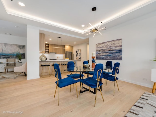 dining space featuring a tray ceiling, a chandelier, and light wood-type flooring