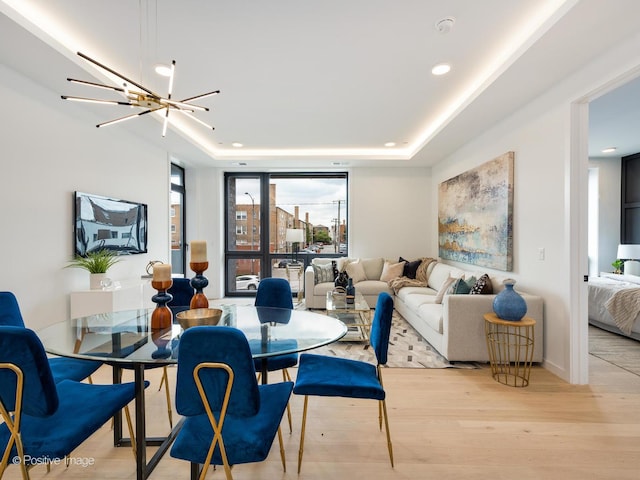 dining area featuring a raised ceiling, a chandelier, and light hardwood / wood-style floors