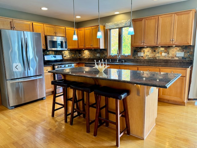 kitchen featuring a kitchen island, appliances with stainless steel finishes, a kitchen bar, and light hardwood / wood-style flooring