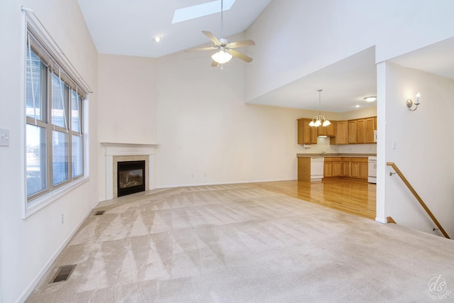 unfurnished living room featuring a skylight, light carpet, high vaulted ceiling, ceiling fan, and a tiled fireplace