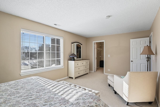 bedroom with a spacious closet, a closet, light colored carpet, and a textured ceiling