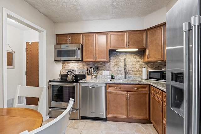 kitchen with sink, tasteful backsplash, light stone counters, light tile patterned floors, and appliances with stainless steel finishes