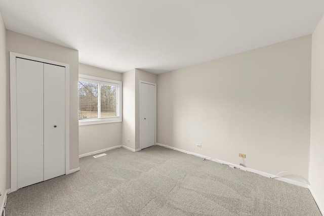 unfurnished bedroom featuring light colored carpet and multiple closets