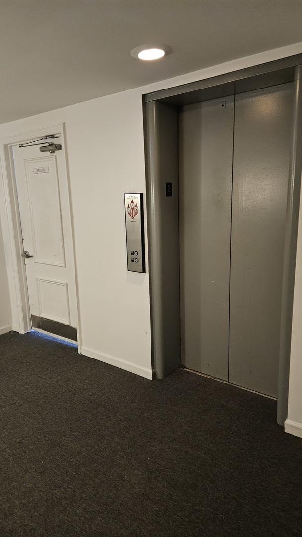 hallway featuring elevator and dark carpet