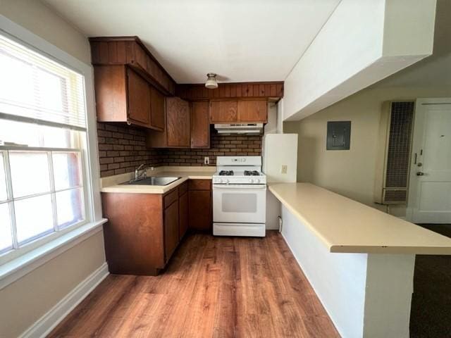 kitchen with gas range gas stove, kitchen peninsula, decorative backsplash, dark hardwood / wood-style flooring, and sink